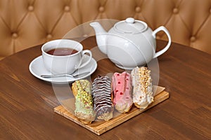 Colorful eclair cakes with cream and teapot on wooden board