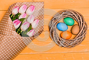 Colorful eggs and bouquet fresh tulip flowers on yellow background top view. Spring holiday. Tradition celebrate easter