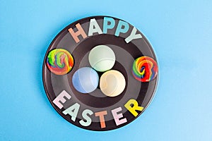 Colorful eggs and marshmallows arranged on black plate.