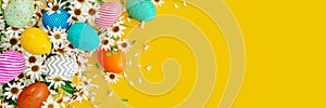 Colorful eggs with white spring flowers and decoration on yellow Easter background