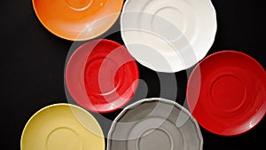 Colorful empty plates and saucers over black background.