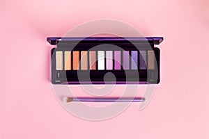 Colorful eye shadow palette and brush on pink background