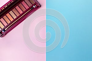 Colorful eye shadow palette in pink colors on blue and pink paper background with copy space. Professional color palette