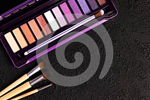 Colorful eye shadow palette and set of makeup brushes on black background