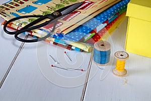 Colorful fabrics with vintage scissors, pins, measuring tape and rolling cotton threads on white wooden table