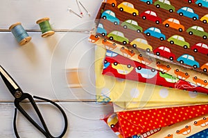 Colorful fabrics with vintage scissors, pins, measuring tape and rolling cotton threads on white wooden table