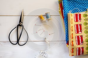 Colorful fabrics with vintage scissors, pins, measuring tape and rolling cotton threads on white wooden table