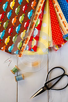 Colorful fabrics with vintage scissors, pins, measuring tape and rolling cotton threads on white wooden table