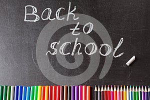 Colorful felt tip pens, pencils and the title Back to school written by white chalk on the black school chalkboard