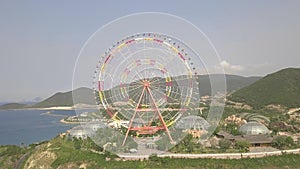 Colorful ferris wheel in amusement park on sea and mountain landscape aerial view. Amusement park with large ferris