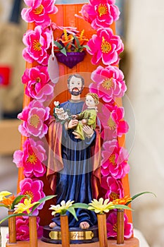 Colorful figure of Saint Joseph holding Child Jesus with pink flowers around