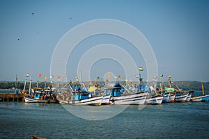Colorful fishing boats with blue and white hulls and Indian flags on the masts, on the fishing pier in Goa. Wooden boats