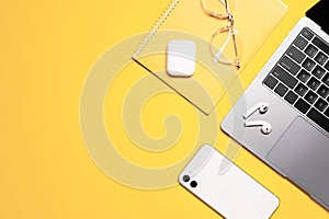 Colorful flat lay photo of a silver grey laptop, white mobile phone, wireless earphones with a case, notebook and stylish goggles