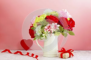 Colorful flower bouquet arrangement with red roses in vase on pink background