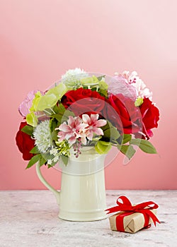 Colorful flower bouquet arrangement with red roses in vase on pink background