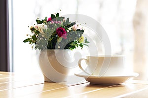 Colorful flowers bouquet in ceramic vase next to cup of tea by the window