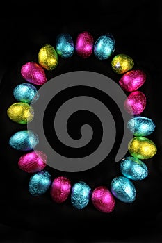 Colorful foil wrapped easter eggs laid out in the oval shape of an egg, on a black background