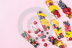 Colorful food snack or dessert from sandwiches with creamy cheese and summer berry fruits on pink trendy background top view.