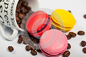 Colorful French delicious macaroons on coffee beans, cup with coffee beans on white background close up