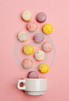 Colorful french macarons fall in white cup on pink background