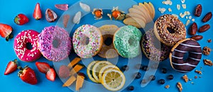 Colorful fresh donuts with different kinds of topping and fruits on blue paper background.