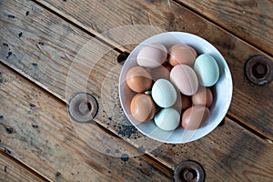 Colorful Fresh Eggs in a white bowl on a wood table