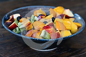 Colorful fresh fruit salad in dark bowl on wooden table in daytime