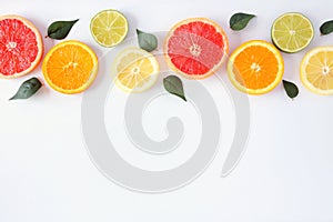 Colorful fruit border of fresh citrus slices with leaves. Top view, flay lay over a white background with copy space