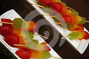 Colorful fruit skewers with strawberries, melons, kiwi, and pineapple on a plate.