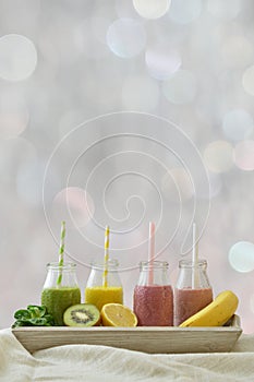 Colorful fruit smoothies in a row with fresh fruits in front of neutral bokeh background
