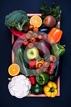 Colorful fruits and vegetables in a wooden box on a dark background