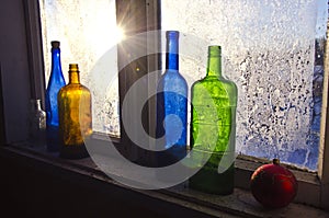 Colorful glass bottles on winter old farm window with hoarfrost ice