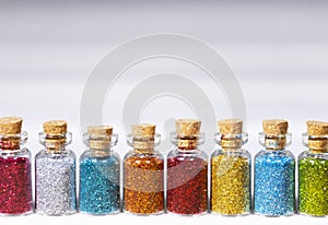 Colorful glitters for nail art and makeup in small glass jars on white background, Coppyspace