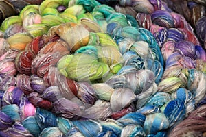 Colorful, handdyed roving of sheepwool, rolled up, natural material ready for spinning on a traditional spinning wheel as a hobby.