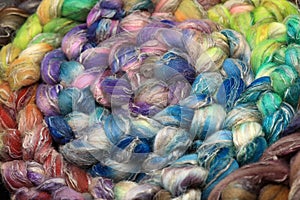 Colorful, handdyed roving of sheepwool, rolled up, natural material ready for spinning on a traditional spinning wheel as a hobby.