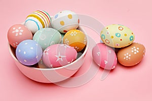 Colorful handmade Easter eggs in bowl and on pink background