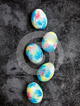 Colorful handmade Easter eggs painted like Earth in row on black marble background. Minimal happy Easter holiday