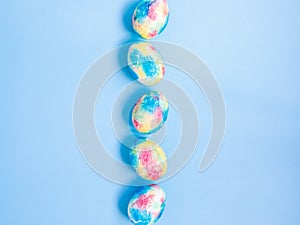 Colorful handmade Easter eggs painted like Earth in row on blue paper background with copy space for your Easter text