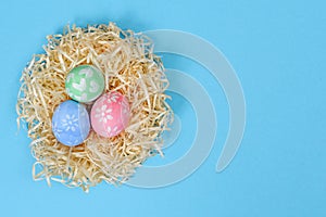Colorful handmade painted Easter eggs in the nest isolated on a blue background. Easter eggs painted by a child