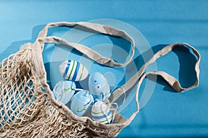 colorful handmade painted easter eggs in a string bag on blue background with hard shadows.