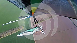 Colorful hangglider wing soars above green cultivated fields