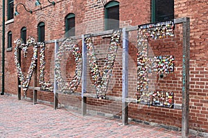 Colorful hanging locks on a love fence with a red wall in background in Toronto in the Distillery District in Canada