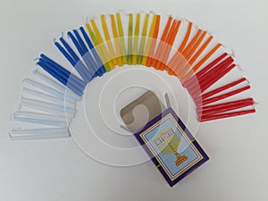 Colorful Hannukah candles creating the shape of a rainbow with a sign of a lamp on the open candle box