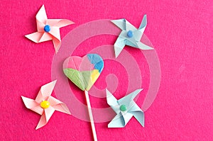 A colorful heart shape lollipop with colorful pinwheels on a pink background