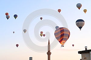 Colorful hot air balloons in the early morning over the town of GÃ¶reme with the tower of a Minaret right next to it, GÃ¶reme,