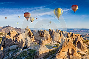 Colorful hot air balloons fly in blue sky over amazing rocky valley in Cappadocia, Turkey