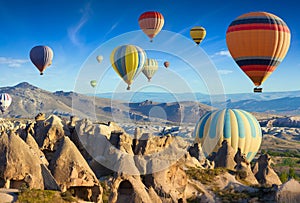 Colorful hot air balloons fly in blue sky over amazing rocky valley in Cappadocia, Turkey