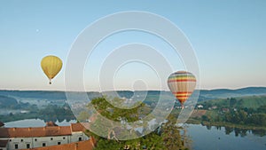 Colorful hot air balloons fly over the medieval castle and lake in the morning fog. Maneuverable flight and power loop