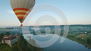 Colorful hot air balloons fly over the medieval castle and lake in the morning fog. Maneuverable flight. Travel