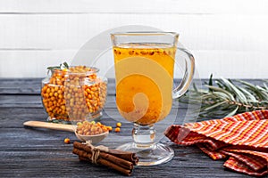 Colorful hot natural sea buckthorn tea in a glass cup, fresh raw berries  and cinnamon sticks. Vitaminic healthy medicine drink.